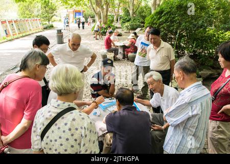 Les Chinois jouent Mahjong dans le parc public de la place du peuple tandis que d'autres les regardent jouer, Shanghai. Banque D'Images