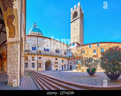 Panorama de la cour du Palazzo Broletto avec tour d'horloge historique en galets, fontaine en pierre, plantes vertes en pots et vue sur la Nouvelle cathédrale (Duomo Nuo Banque D'Images