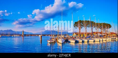 Le panorama en soirée du port de Desenzano del Garda sur le lac de Garde avec yachts amarrés, petits bateaux, vieux phare en pierre et remblai de la vieille ville Banque D'Images