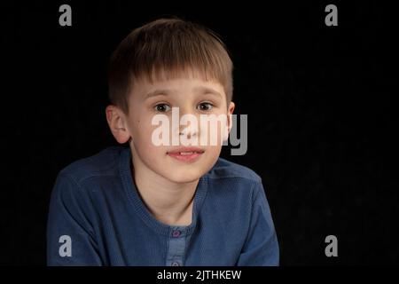 Portrait d'un garçon de dix ans sur fond sombre. L'enfant regarde dans la caméra avec des yeux intelligents. Beau garçon d'âge scolaire. Banque D'Images