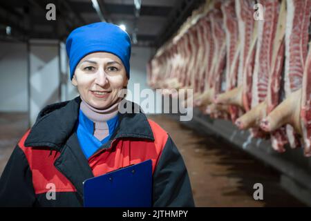 Travailleur de l'usine d'emballage de la viande devant les carcasses bouchées. Production de viande. Un boucher professionnel entre les rangées de carcasses de porc, regardant le venu Banque D'Images