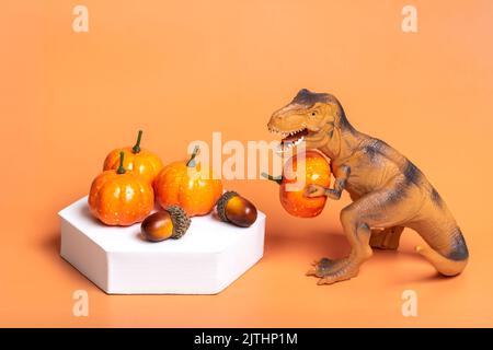 Jouet dinosaure Tyrannosaurus tenant le potiron dans ses pattes, sur le podium blanc isolé sur fond orange carte de voeux de vacances Joyeux jour d'Halloween, Bonjour Banque D'Images