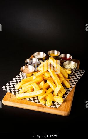 Frites sur une table en bois accompagnées de différents types de sauces sur fond noir Banque D'Images