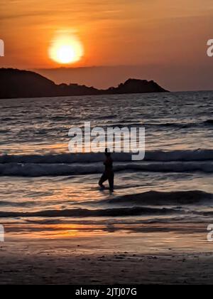 Personne est silhouetté contre le coucher du soleil comme ils marchent le long de la plage de Kata Beach, Phuket, Thaïlande. Banque D'Images