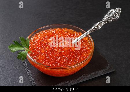 Bol de caviar de saumon kéta sur fond d'ardoise noire. Caviar rouge à la truite et cuillère vintage dans un bol en verre en gros plan. Spécialités de poisson et de fruits de mer. Vue de dessus. Banque D'Images