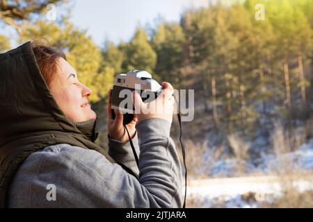 Photo de côté d'un womanphotographe avec l'appareil photo prendre la photo d'une merveilleuse journée d'hiver ensoleillée avec les yeux fermés. Banque D'Images