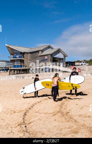 Les jeunes surfeurs et leur instructeur portant leurs planches de surf au début de leur cours de surf sur Fistral Beach à Newquay en Cornouailles en Angleterre i Banque D'Images