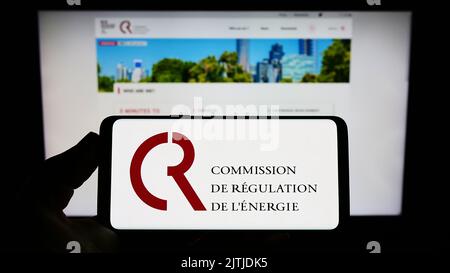 Personne tenant un smartphone avec le logo de la Commission française de régulation de l'Energie (CRE) à l'écran devant le site. Mise au point sur l'affichage du téléphone. Banque D'Images