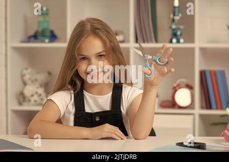 bonne fille tient des ciseaux dans la salle de classe de l'école Banque D'Images