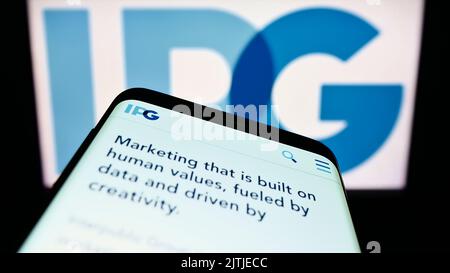 Téléphone mobile avec page Web du Groupe Interpublic des compagnies Inc. (IPG) à l'écran devant le logo de l'entreprise. Faites la mise au point dans le coin supérieur gauche de l'écran du téléphone. Banque D'Images
