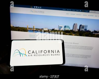 Personne tenant un téléphone portable avec le logo du California Air Resources Board (CARB) à l'écran devant la page Web. Mise au point sur l'affichage du téléphone. Banque D'Images