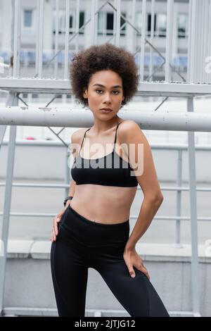 brunette afro-américaine femme en soutien-gorge de sport noir et leggings posant les mains sur les hanches Banque D'Images