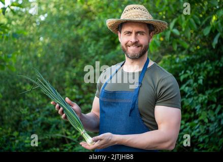 happy man greengrocer dans un chapeau de paille avec un légume d'oignon vert Banque D'Images