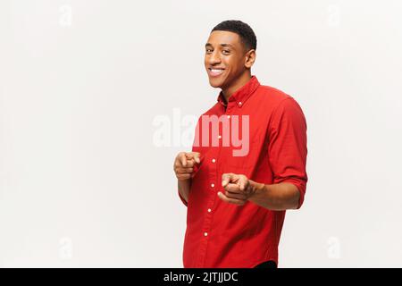 Un homme hispanique insouciant dans des danses de chemise rouge isolé sur blanc. L'homme latin surjoyeux danse, fait des mouvements à la musique, sourit positivement, étant dans l'esprit élevé Banque D'Images