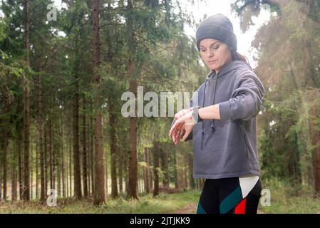 femme vérifiant le tracker de la montre intelligente. Trail running coureur fille regardant le moniteur de fréquence cardiaque montre intelligente dans la forêt. Entraînement de jogging d'athlète féminine Banque D'Images