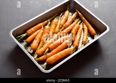 Carottes glacées au miel rôties sur plaque de cuisson sur fond de pierre sombre. Vue rapprochée Banque D'Images