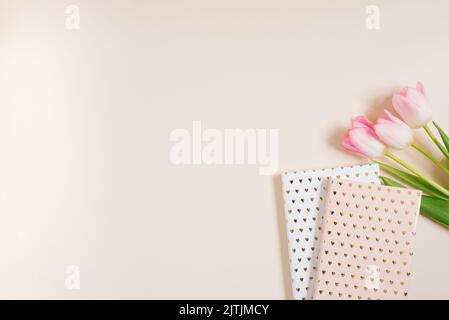 Carnets et un bouquet de fleurs de tulipe roses. Lieu de travail d'une femme blogueuse. Flat lay, vue de dessus, espace de copie Banque D'Images