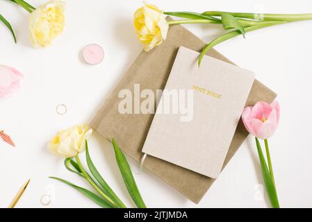 Le lieu de travail des femmes avec un carnet, des fleurs de tulipe roses et jaunes, un stylo, des cahiers. Le concept d'entreprise du blogueur. Position plate, vue de dessus. Banque D'Images