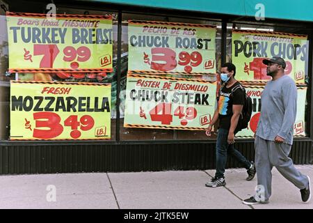 Deux hommes afro-américains marchent devant les fenêtres de devant affichant les prix des produits alimentaires dans Edgewater Produce à Chicago, Illinois, en juillet 2022. Banque D'Images