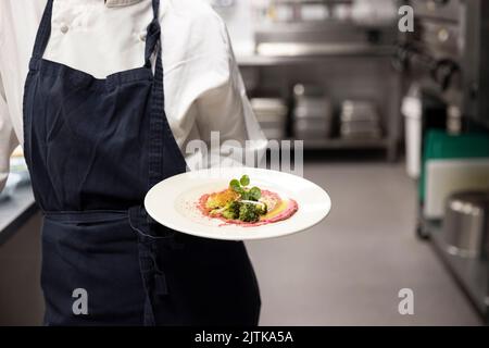 Section intermédiaire du chef transportant des plats prêts à manger dans l'assiette de la cuisine du restaurant Banque D'Images