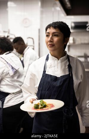 Femme chef transportant une assiette de nourriture tout en marchant dans la cuisine du restaurant Banque D'Images