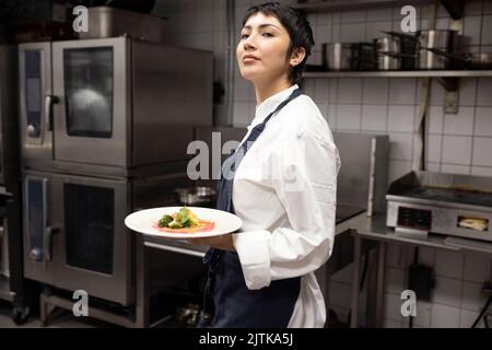 Chef marchant avec la nourriture dans l'assiette dans la cuisine commerciale Banque D'Images