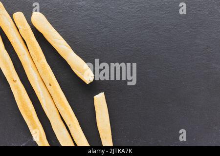 Gressins italiens frais Grissini servis sur fond noir. Pain cuit à sec avec des morceaux d'olive sur une assiette d'ardoise. Vue de dessus, espace de copie Banque D'Images