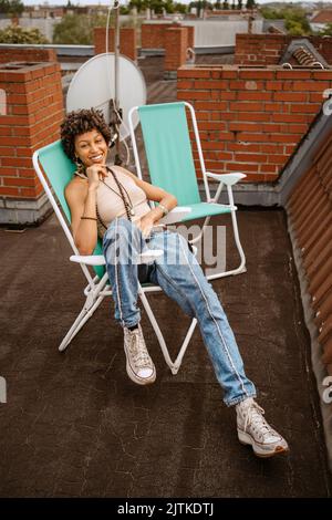 Portrait complet de jeune femme souriante assise sur une chaise sur le toit Banque D'Images