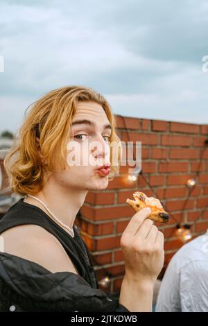 Portrait d'un jeune homme blond avec des lèvres de pizza puckering sur le toit Banque D'Images