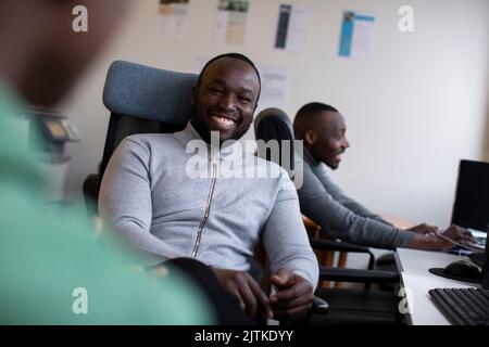 Portrait d'un homme d'affaires gai assis sur une chaise avec ses collègues au bureau Banque D'Images