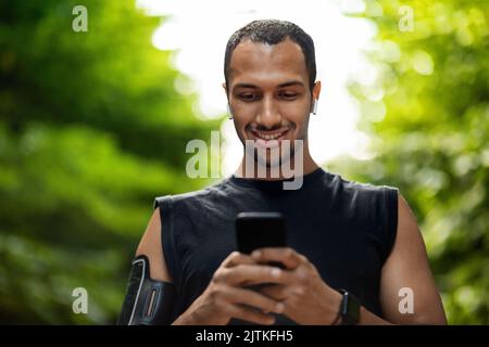 Beau sportif noir s'entraîner au parc, à l'aide d'un smartphone Banque D'Images