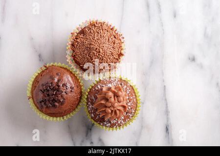 Trois cupcakes au chocolat différents, tournés d'en haut, sur fond de marbre gris avec espace pour les copies Banque D'Images