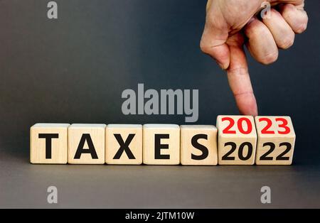 symbole 2023 taxes nouvel an. Homme d'affaires transforme un cube en bois et change les mots impôts 2022 en impôts 2023. Magnifique fond gris de table, Copy spa Banque D'Images