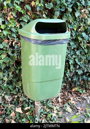 Plan vertical sur un panier public en plastique vert pour l'élimination des déchets contre un mur avec de la lierre verte Banque D'Images