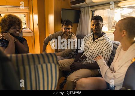 Groupe interracial de quatre bons amis sur une route d'été, assis dans leur confortable motorhome moderne, bavardant et relaxant. Intérieur du RVS. Photo de haute qualité Banque D'Images