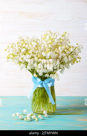 bouquet de lys de la vallée dans un vase avec ruban bleu sur fond de bois bleu et blanc Banque D'Images