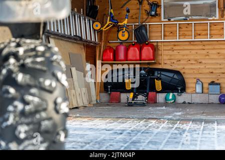 Vue de fond en gros plan de quad offroad véhicule garée garage de la maison ouverte porte sur la neige ensoleillée froid hiver jour. Pelle à déneiger Banque D'Images