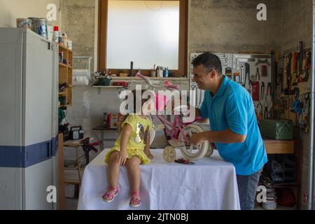 Image d'un père avec sa fille dans le garage à la maison comme ils réparent et s'adaptent les roues sur un vélo rose pour enfants. Banque D'Images