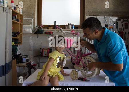 Image d'un père avec sa fille dans le garage à la maison comme ils réparent et s'adaptent les roues sur un vélo rose pour enfants. Banque D'Images