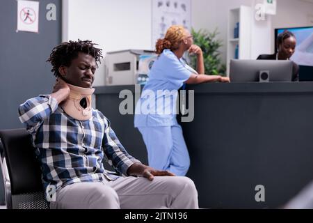 Homme avec col cervical à la réception, demandant de l'aide et d'être dans la douleur. Patient avec un renfort en mousse médicale attendant d'assister à un rendez-vous d'examen de contrôle pour guérir la blessure après accident. Banque D'Images