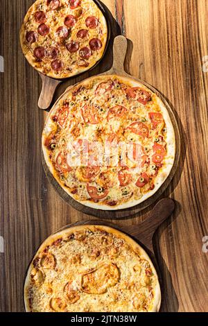 Trois pizzas aux saveurs différentes. Pepperoni, fromage, pomme de terre, oignon, tomate. Pizza italienne de qualité. Banque D'Images