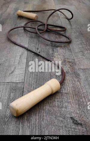 Ancienne corde à sauter en cuir avec poignées en bois enroulées sur un plancher en bois Banque D'Images