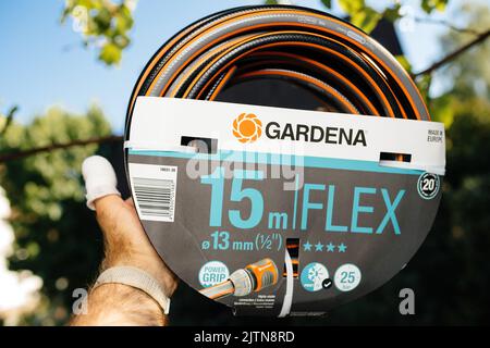 Francfort, Allemagne - 16 juillet 2022: POV main mâle tenant nouveau Gardena 15 mètres Flex power grip tuyau de jardin - vert défoqué sur fond de vignoble Banque D'Images