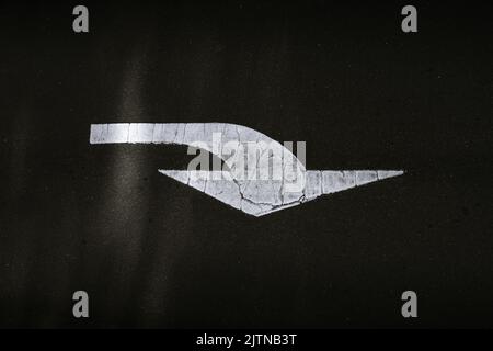 Panneau de route à flèche courbée peint sur la route asphaltée au bitume en peinture blanche. Photographié d'en haut. Certains intempéries, usure et déchirure sont visibles dans le r Banque D'Images