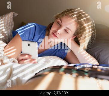 Les réseaux sociaux ne dort jamais. Une jeune femme détendue utilisant son smartphone tout en étant au lit à la maison. Banque D'Images
