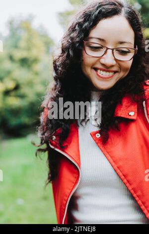 Femme brune souriante, portant une veste en cuir rouge dans la nature. Banque D'Images
