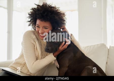 Il veut juste se câliner. Une jeune femme attrayante qui pille son chien tout en étant assise sur le canapé à la maison. Banque D'Images