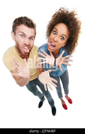 Devenir un peu fou. Portrait en studio d'un jeune couple tirant les visages de la caméra sur un fond blanc. Banque D'Images