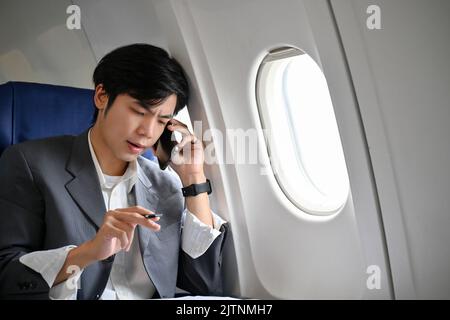 Homme d'affaires asiatique stressé et professionnel ayant un appel téléphonique sérieux avec quelqu'un pendant le vol à une réunion d'affaires. Banque D'Images