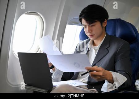 Homme d'affaires asiatique prospère se concentrant sur le travail, préparant des documents de réunion, lisant un rapport pendant le vol pour son voyage d'affaires. Entreprise Banque D'Images